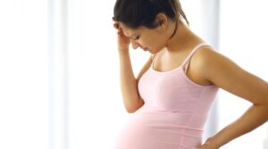 Mulher grávida com perna inchada, indicando possível trombose, ou com expressão de preocupação.